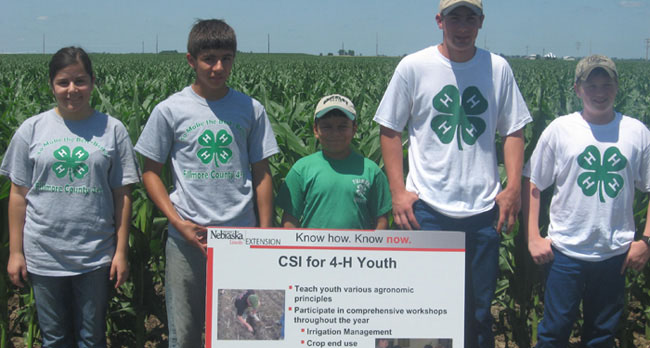 CSI youth holding sign in front of corn rows