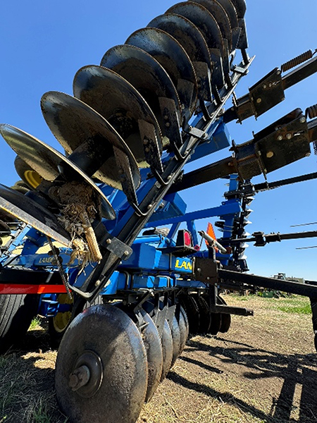 Large agricultural disc harrow with metal blades, set against a clear blue sky.