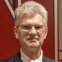 Man in formal attire, standing in front of red and tan wall panels.