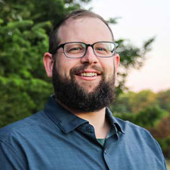 Headshot of Nick Arneson in blue collared shirt smiling in an outdoors photo