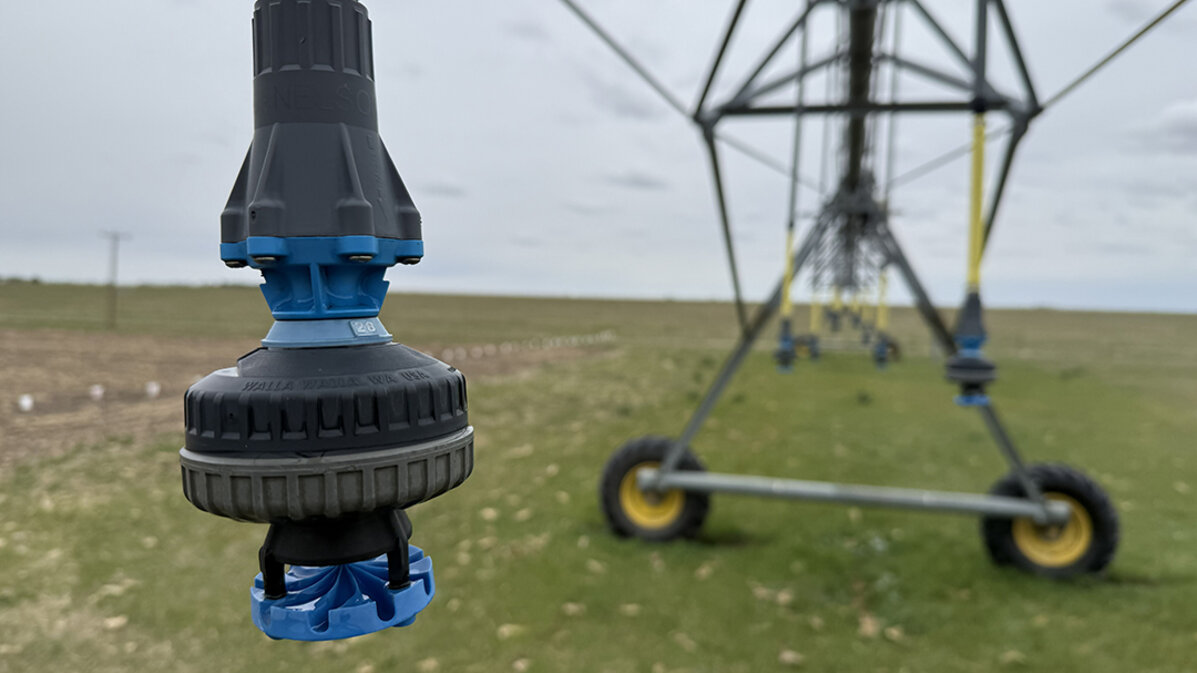 Sprinkler nozzle on an irrigation system in a grassy field under a cloudy sky.