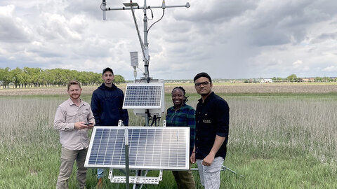 four people stand around weather station in field