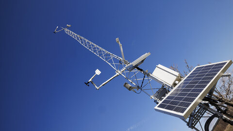 A Nebraska Mesonet weather station with solar panels and meteorological sensors extends into a clear blue sky.