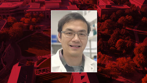 Color portrait of Huang Li, research assistant professor of biochemistry and Heuermann Research Fellow at the University of Nebraska–Lincoln, on a red campus background.