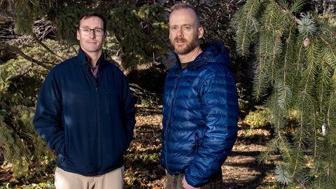 Kyle Dougherty and John Benson stand among trees in winter gear.