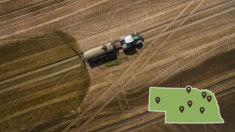 Aerial view of a tractor pulling a manure tanker applying liquid manure across a harvested field, with a Nebraska map overlay showing multiple workshop locations.
