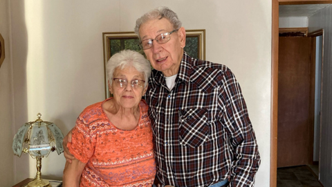 Don and Mary Lee Gasper stand side by side and smile for a photo inside their home