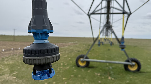 Sprinkler nozzle on an irrigation system in a grassy field under a cloudy sky.