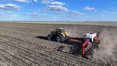 Tractor pulling a red planter across a dry, residue-covered field, kicking up dust under a blue sky with scattered clouds.