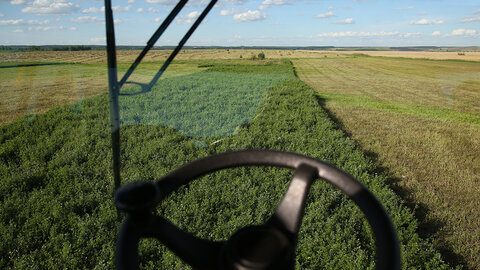 Farm field view through a tractor window, green crops and blue sky visible.