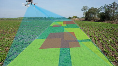  A drone equipped with sensors flies over a crop field, projecting a scanning beam that maps the field with overlaid color-coded zones indicating variations in crop health or soil conditions.