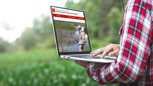 Man searching pesticide training website on laptop in field