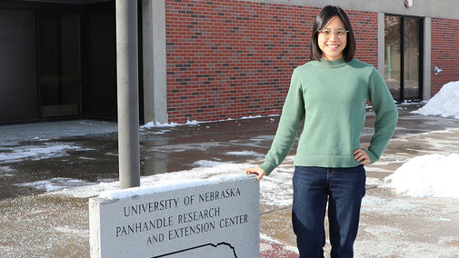 Pin-Chu Lai stands in front of extension building near sign