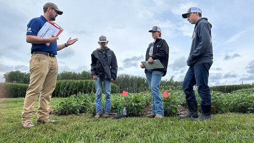 Adult speaks to three youth in field