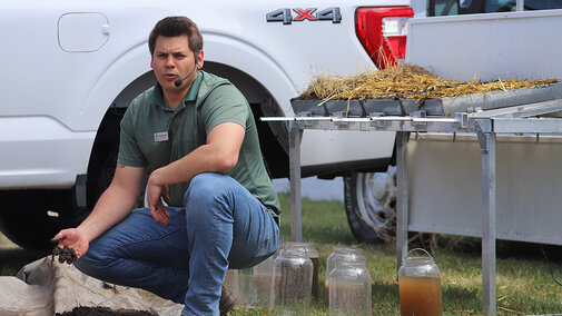 Man squats near demo table while speaking