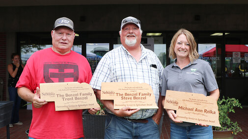 Trent Benzel, left, Steve Benzel and Michael Ann Relka stand with plaques