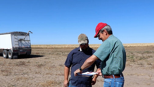 Men standing in field looking at clipboard