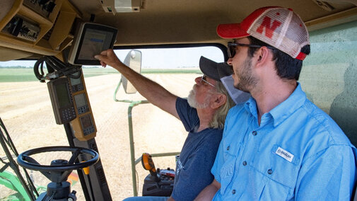 Two men inside tractor cab looking at software interface