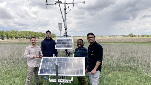 four people stand around weather station in field