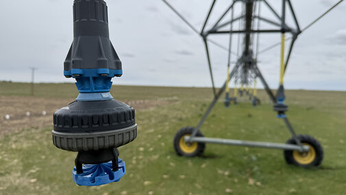 Sprinkler nozzle on an irrigation system in a grassy field under a cloudy sky.