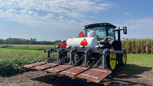 Tractor with sprayer attachment in a field under a cloudy sky.