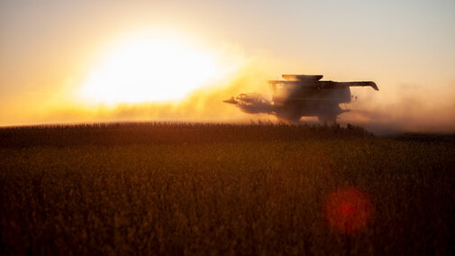 Combine harvester in a field at sunset, surrounded by dust.