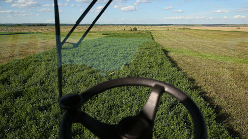 Farm field view through a tractor window, green crops and blue sky visible.