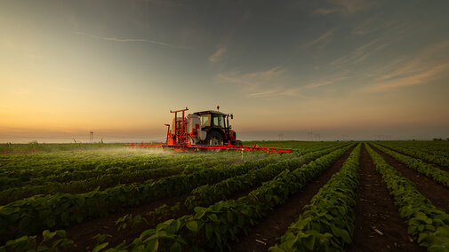 Farmer applies pesticide to soybean crop near dusk during spring