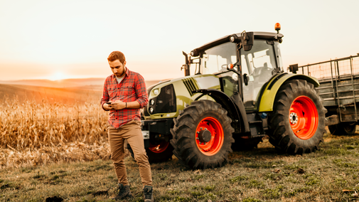 man using phone near corn field and tractor