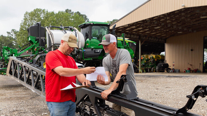 two men looking at paperwork near farm equipment