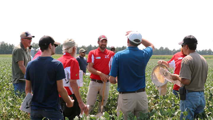 A group of farmers and Nebraska Extension educators stand in a soybean field, discussing crop management during a summer field day event.