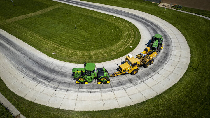 A green tractor pulls a yellow test car and an additional green tractor for weight as it rounds a test track.
