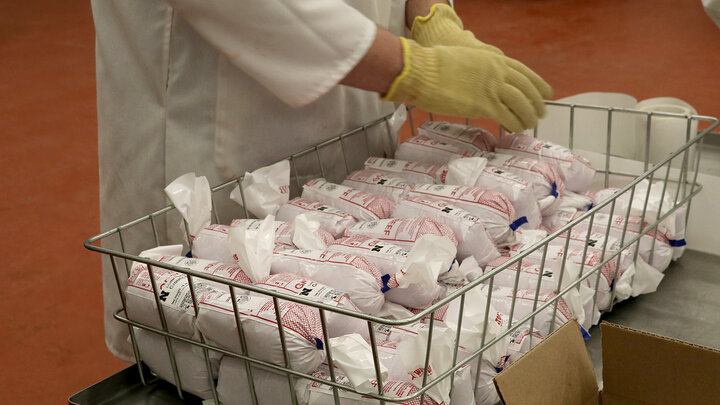 A person wearing a labcoat and yellow gloves packages rolls of ground beef.