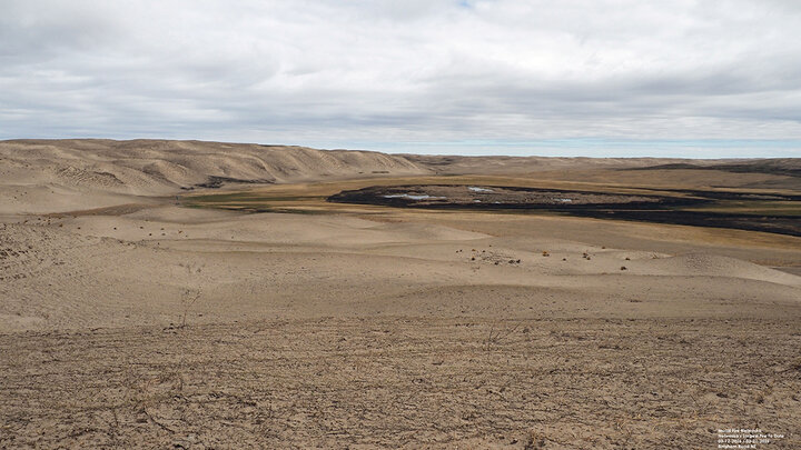 Expansive barren landscape with sandy hills, sparse vegetation, and cloudy sky.