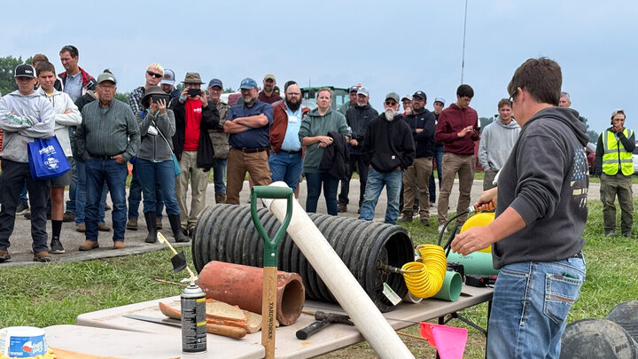 A person demonstrating tools to a large group outdoors under a cloudy sky.