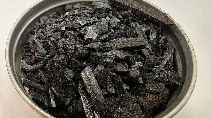 Close-up of a metal container filled with jagged, black pieces of biochar made from eastern redcedar.