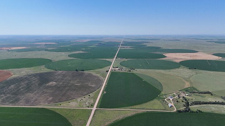 Aerial view of Nebraska farmland with circular center-pivot irrigation fields, intersecting roads and farm buildings under a clear blue sky.