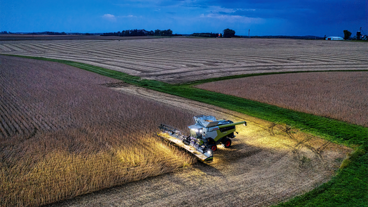 lights glow on combine into soybean field during harvest at dusk
