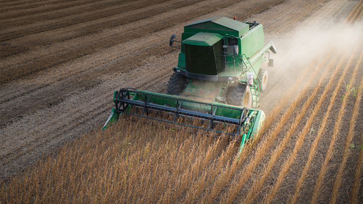 Green combine kicks up dust as it harvests soybean field