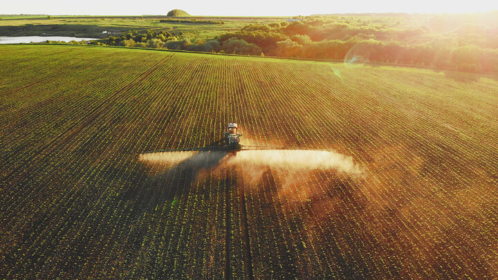 aerial photo of tractor applying pesticide as it drifts across young soybean field in late afternoon