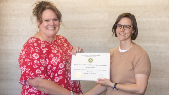 Two women smile at camera and shake hands while holding certificate