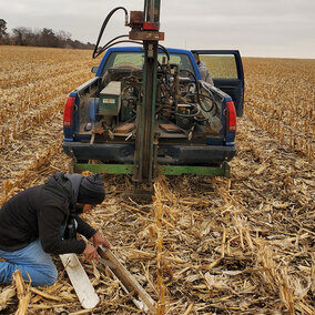 Researcher kneels in field to gather sample