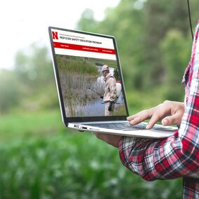 Man searching pesticide training website on laptop in field