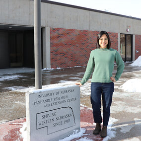 Pin-Chu Lai stands in front of extension building near sign