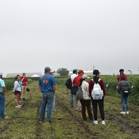 People gather at field's edge to listen to presentation