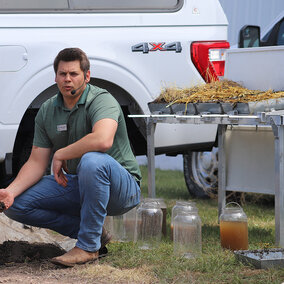 Man squats near demo table while speaking