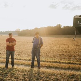 Three people stand in field near equipment