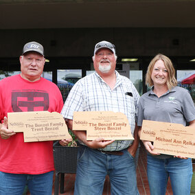 Trent Benzel, left, Steve Benzel and Michael Ann Relka stand with plaques