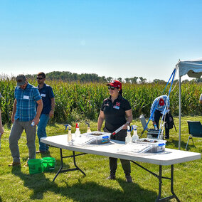 Woman stands at table in front of field day attendees near field