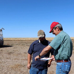 Men standing in field looking at clipboard